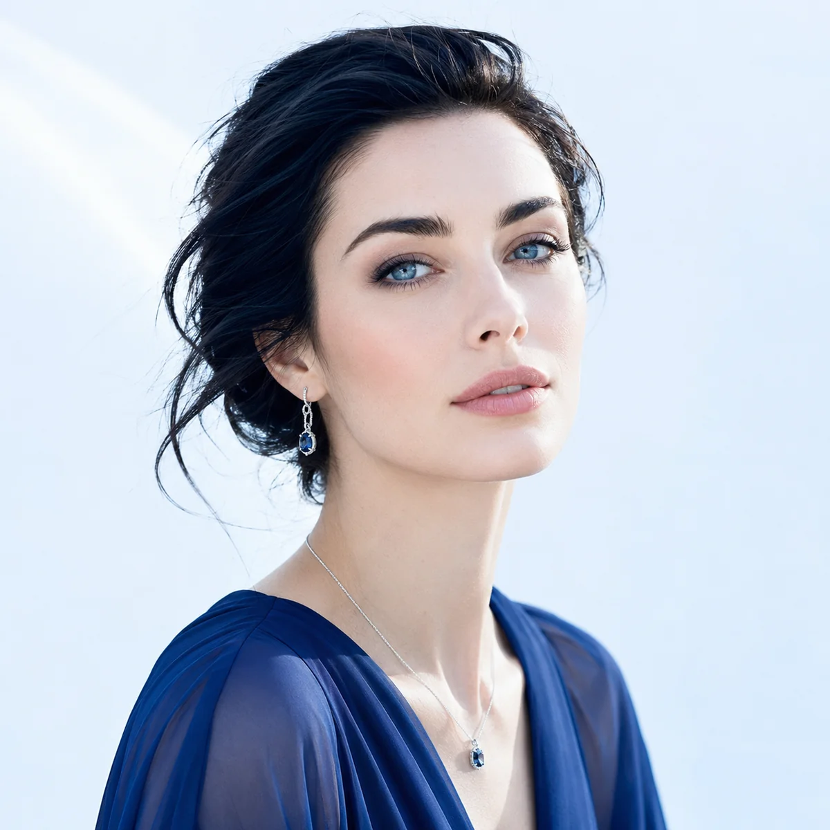 A woman with cool, clear winter coloring glowing in a sapphire blue top with silver jewelry against a bright icy background
